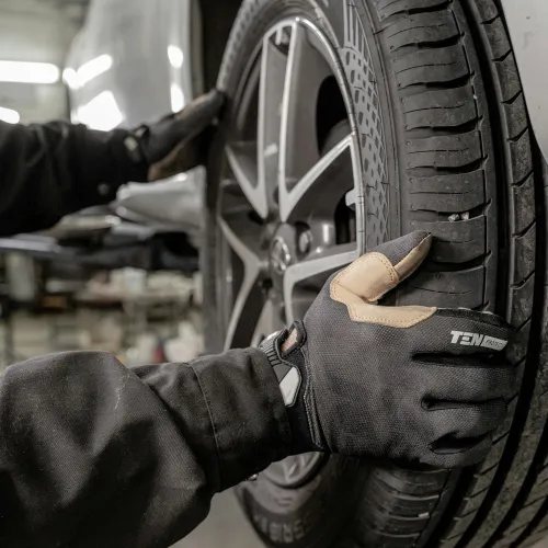 Mechanic with gloves installing or inspecting a car tire and alloy wheel in an auto repair shop.