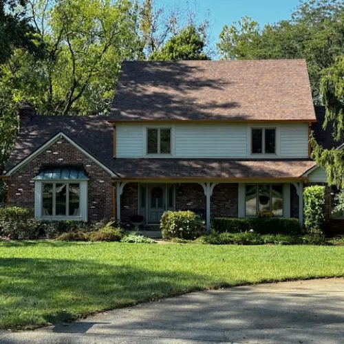 Charming suburban house with brick and siding, surrounded by greenery and a well-kept lawn in a sunny neighborhood.