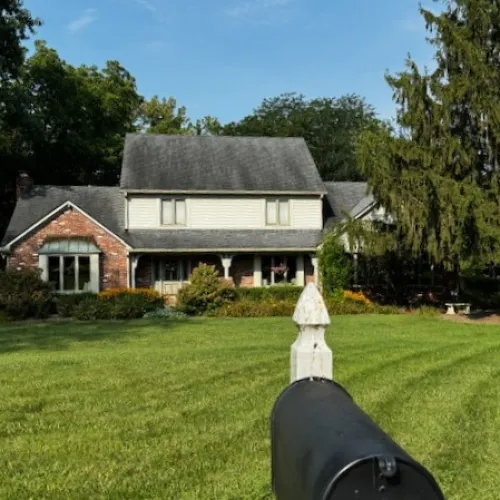 Charming suburban home with a large yard and mature trees under a clear blue sky.