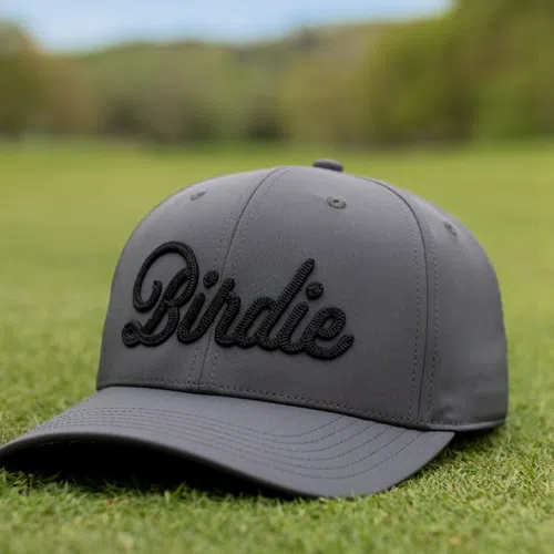 Gray baseball cap with the word Birdie embroidered in black script on the front, resting on green grass.