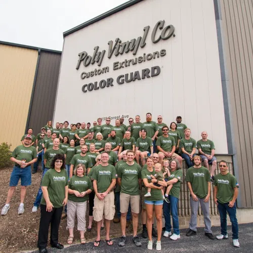 Large group of Poly Vinyl Co. employees wearing green shirts standing in front of company building with signage.