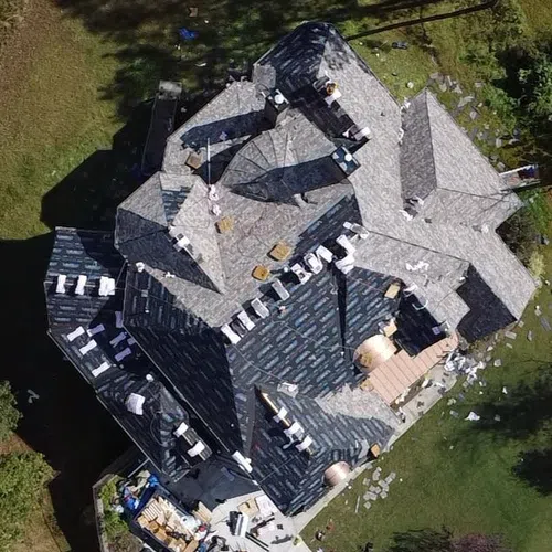 Aerial view of a large house roof under construction with roofing materials and equipment scattered around.