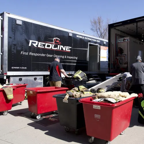 First responders cleaning and inspecting gear outside Redline mobile extraction units with bright red carts on a sunny day