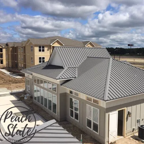Modern residential building with metal roofing installation under a cloudy sky in a developing neighborhood.