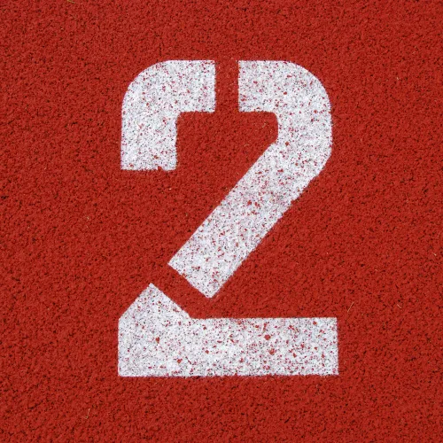 White number 2 painted on a red textured running track surface, marking a lane or position.
