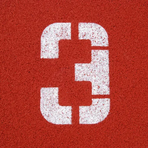 White number 3 painted on a red textured running track surface.