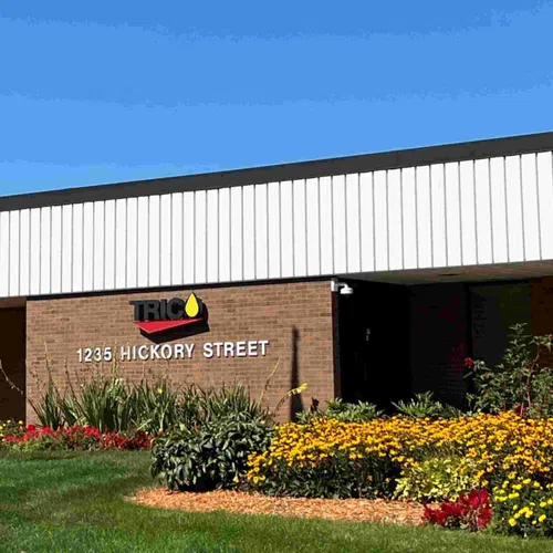 Brick building at 1235 Hickory Street with TRIC logo and vibrant flower garden under a clear blue sky.