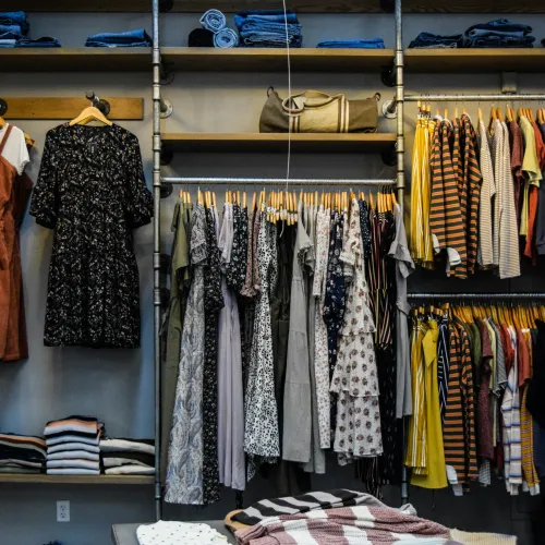 Clothing store display with dresses, tops, folded jeans, and accessories on shelves and racks.