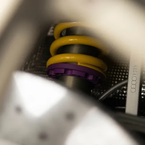 Mechanic with gray cap working on yellow car suspension and brake system inside red vehicle wheel well.