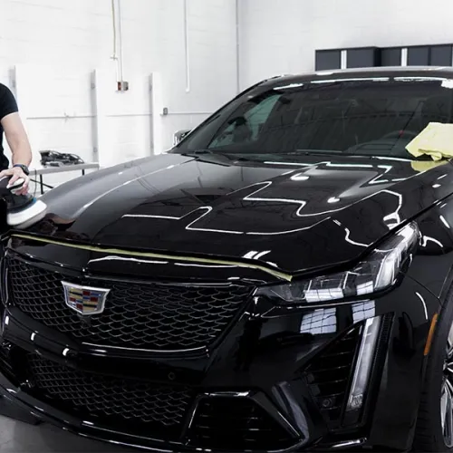 Person polishing a shiny black Cadillac car inside a clean garage or detailing shop.