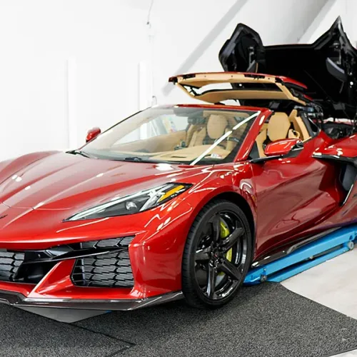 Red convertible sports car with black wheels and tan interior in a bright garage with roof partially open