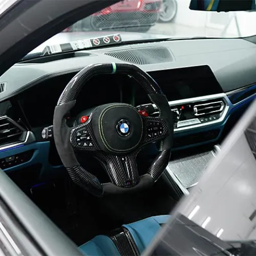 Interior view of a BMW car showcasing a sporty carbon fiber steering wheel and modern dashboard design.