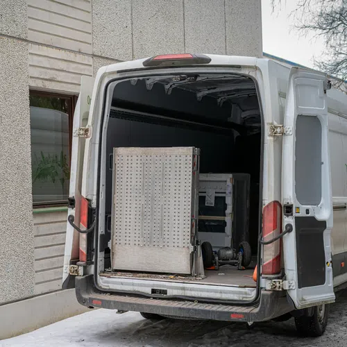 White delivery van with open rear doors parked by building with equipment inside and snow on ground