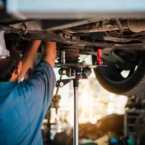 Mechanic working under a car lifted on a hydraulic lift in an auto repair shop with tools around.
