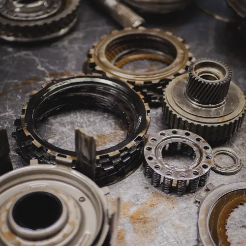 Mechanic wearing gloves tightening engine part with a wrench under a car hood in a workshop.