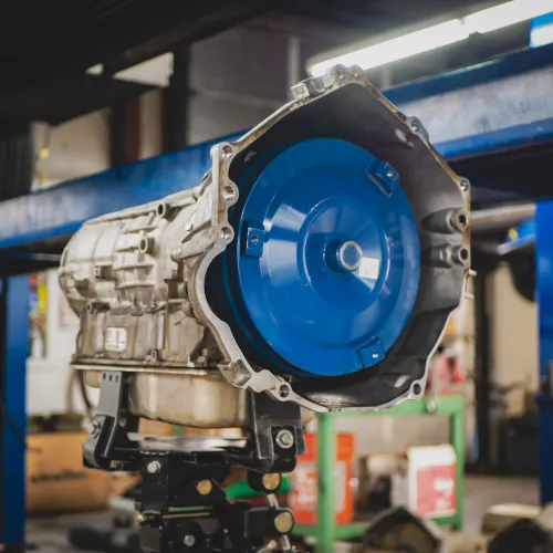 Close-up of a car transmission on a stand in an automotive repair shop with tools and equipment in background