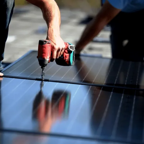 Worker using a drill to install solar panels on a rooftop under sunny conditions