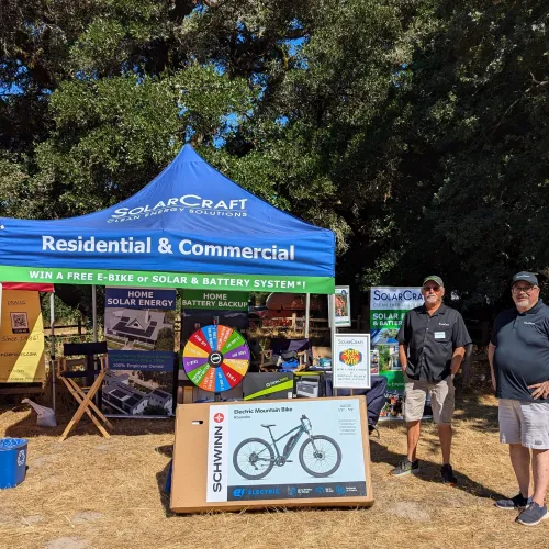SolarCraft booth at outdoor event promoting residential and commercial solar energy and battery systems with prize wheel and electric bike.