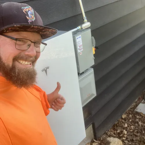 Man smiling and giving thumbs up next to Tesla Powerwall installed on house exterior wall