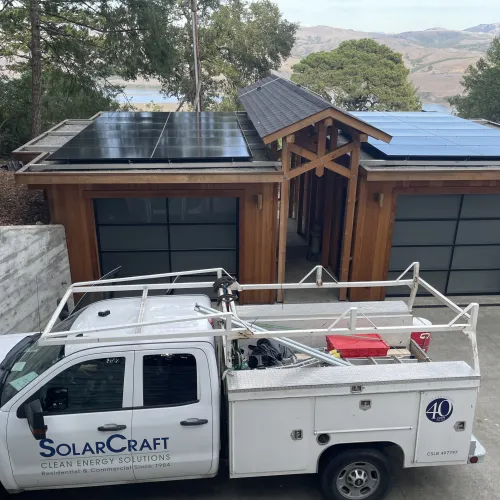 White SolarCraft service truck parked outside a modern home with solar panels on the roof surrounded by trees and hills.