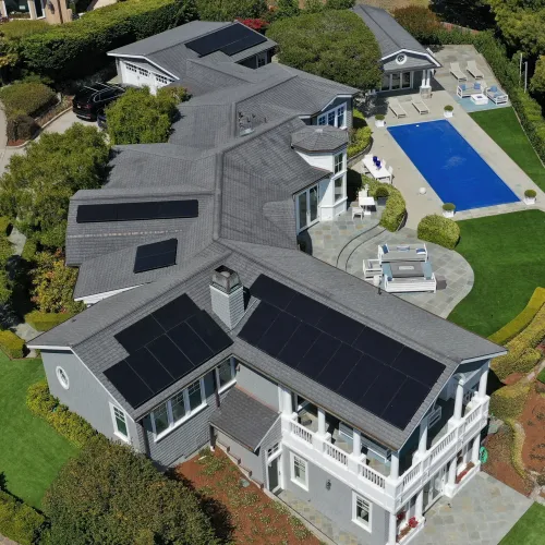 Aerial view of a large modern house with solar panels on roof, a swimming pool, patio, and landscaped garden.