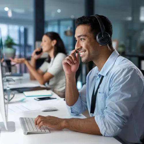 Smiling customer support agent wearing headset working at computer in modern office environment