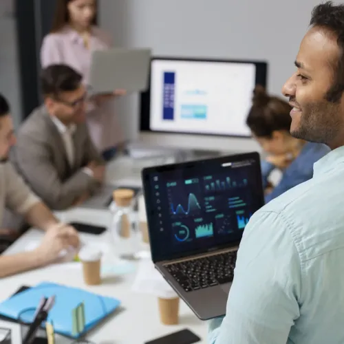 Man presenting data analytics on laptop to team in modern office meeting room.