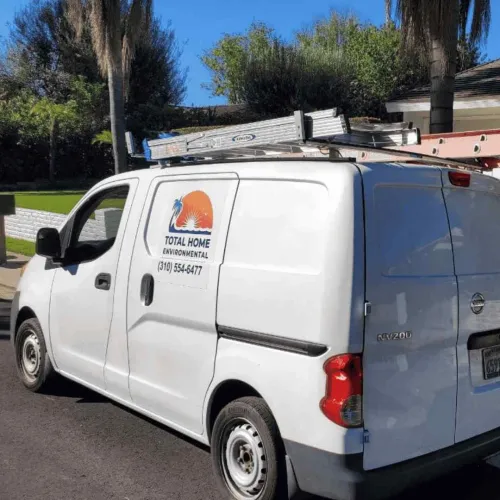 White Total Home Environmental service van with ladders on roof parked on residential street