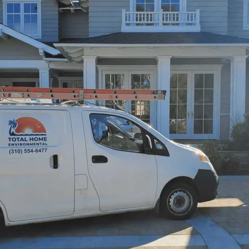 White utility van with ladder parked outside a modern gray house with large windows and white trim.