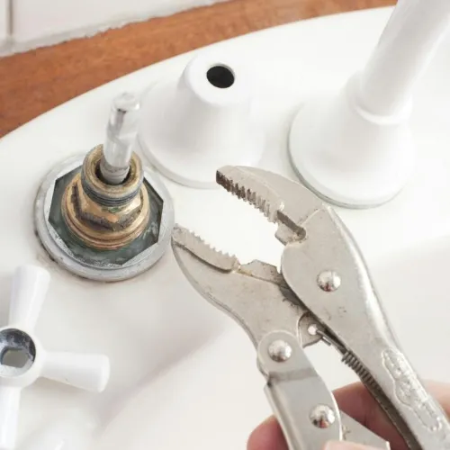 Close-up of a sink faucet being repaired with adjustable pliers removing the handle mechanism.