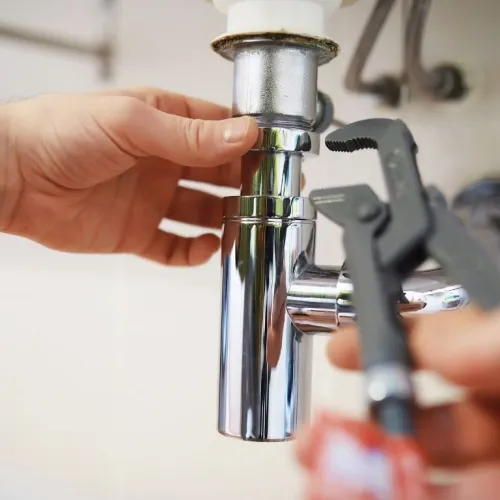 Hands repairing a shiny chrome plumbing pipe under a sink using a wrench tool