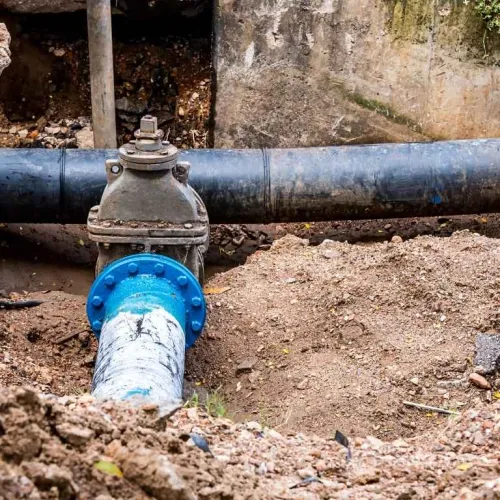 Blue and black underground water pipes with a valve installed in a dirt trench for maintenance.