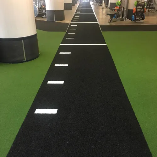 Black turf running track with white markings inside a gym surrounded by green flooring and equipment.