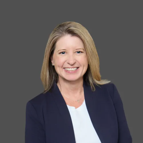 Professional woman with blonde hair wearing navy blazer and white top smiling against gray background