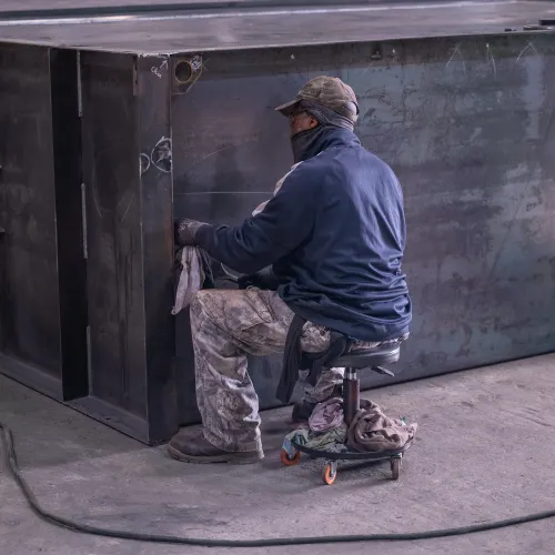 Worker in protective gear inspecting large UL-142 fuel storage tank in industrial setting.