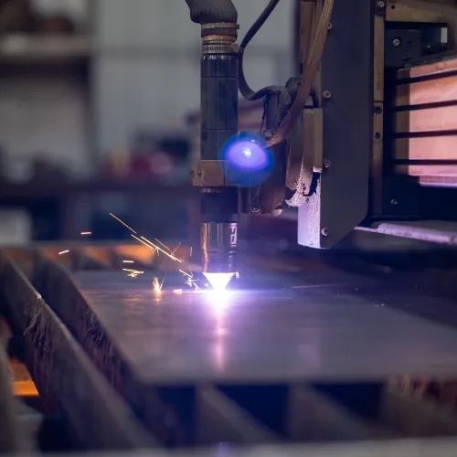 Close-up of a CNC plasma cutting machine slicing through a metal sheet with sparks flying.