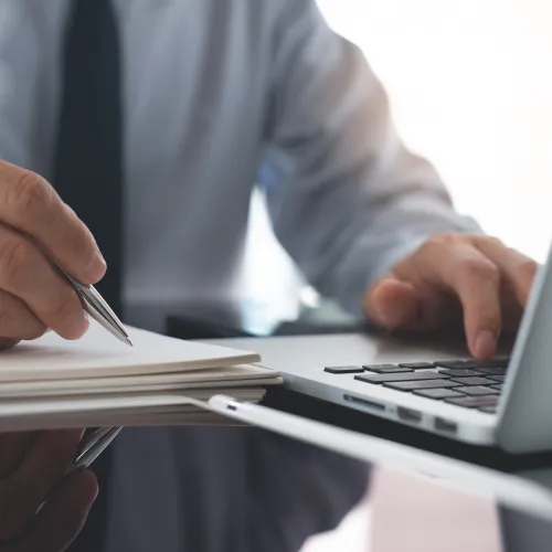 a close-up of a man writing next to a laptop