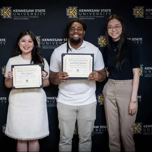 Four people standing in front of Kennesaw State University banner, two holding School of Accountancy certificates.