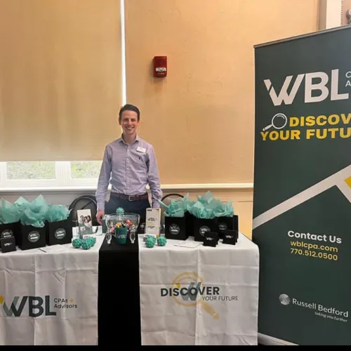 Smiling man stands at WBL CPAs and Advisors booth with branded giveaways and Discover Your Future banners