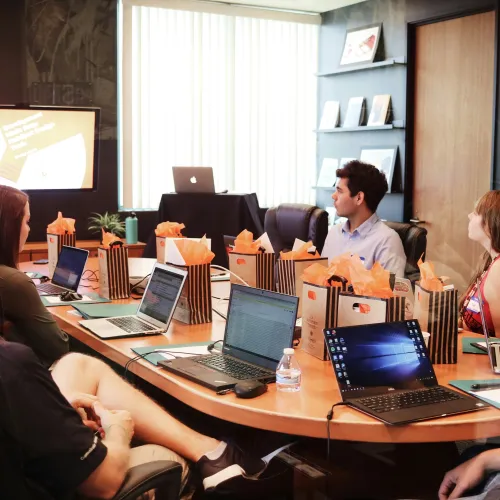 Team members attending a business presentation in a modern conference room with laptops and gift bags
