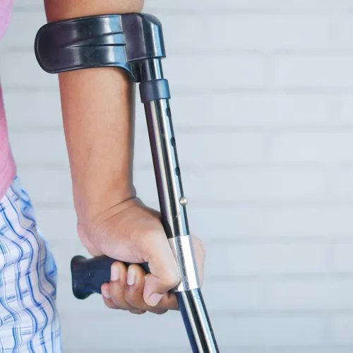 Close-up of a person using a metal forearm crutch with an adjustable height and black handle.