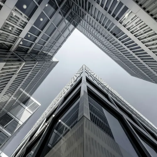 Looking up at modern glass and steel skyscrapers forming an architectural cross against a gray sky.
