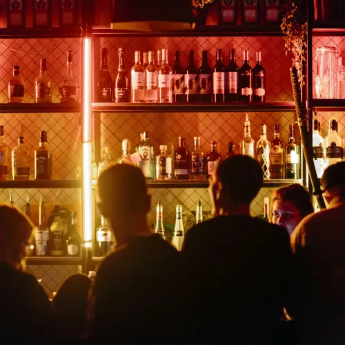 People sitting at a dimly lit bar with illuminated shelves filled with various liquor bottles.