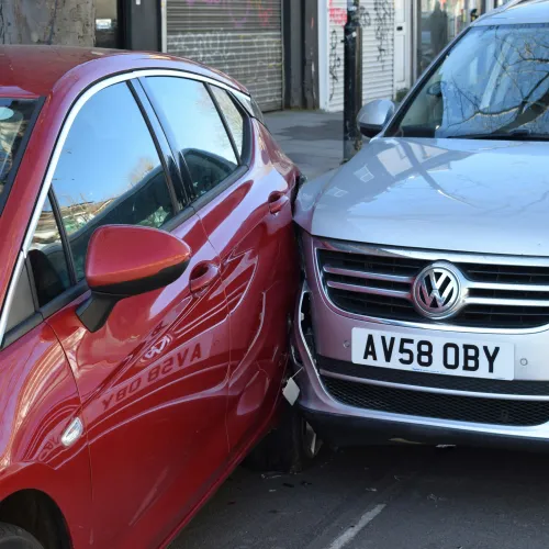 Red car side collides with front corner of silver Volkswagen on urban street.
