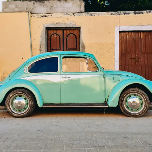 Vintage mint green Volkswagen Beetle parked beside a yellow wall with two wooden doors.