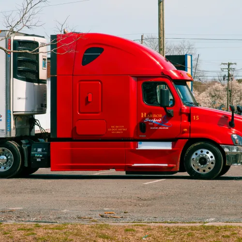 Red semi-truck parked in an outdoor lot with white trailer attached under clear sky