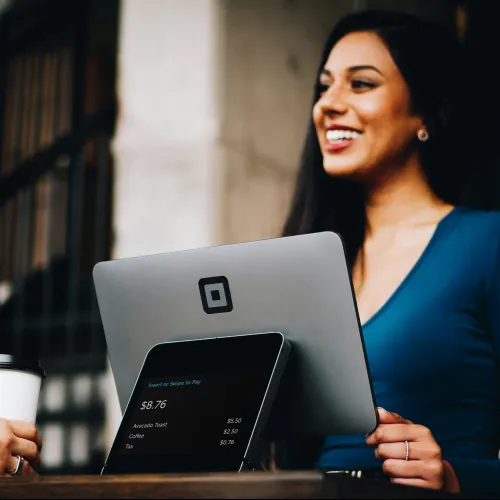 Smiling woman using a Square payment system with customer holding a coffee cup at a cafe counter
