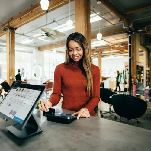 Young woman smiling while making a payment with a credit card at a modern retail store counter.