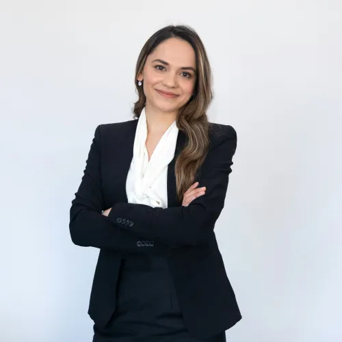 Professional confident woman in black suit and white blouse standing with arms crossed against white background.