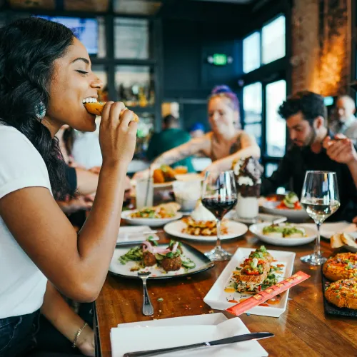 Group of young adults enjoying a meal together at a restaurant with diverse dishes and drinks on the table